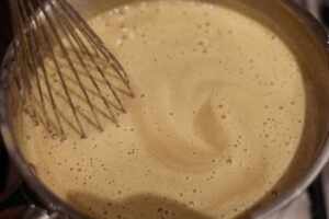 Coffee infused milk based mixture in a metal pan with a whisk sat in it.