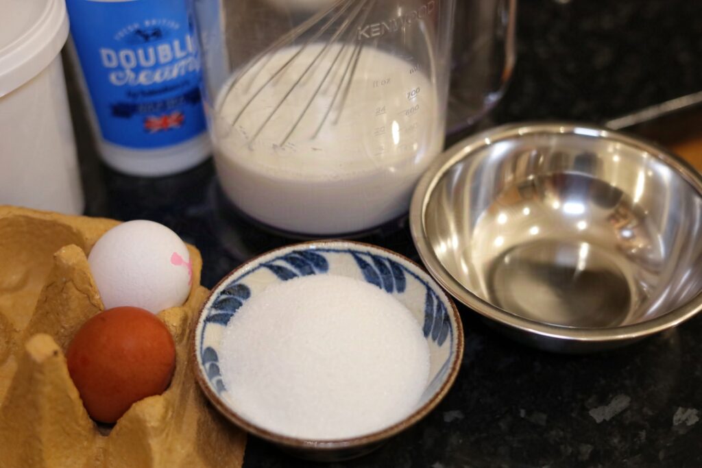 Ingredients. There is cream, eggs, cream, glucose, sugar, milk in a jug with a whisk in it and a bowl ready for the eggs,